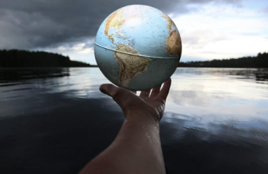 A hand holding a depiction of the globe over water. Photo from Unsplashed.com.  