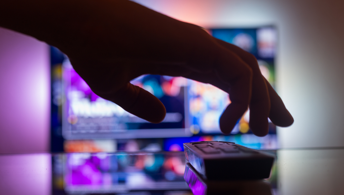 A hand picking up a remote for a TV. Photo by Canva.com.